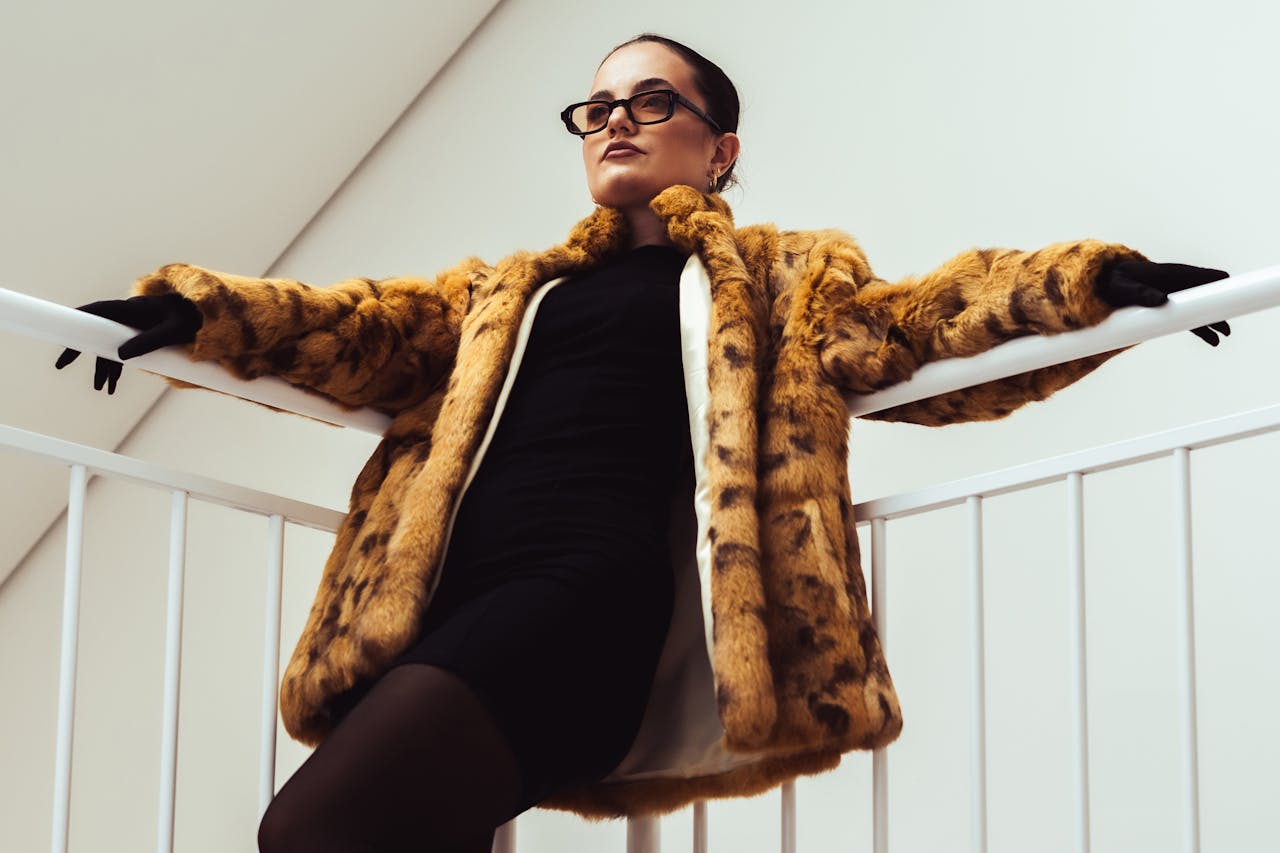 Fashionable adult woman in a leopard print coat posing against a minimalist indoor backdrop.